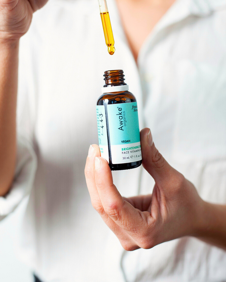 Person holding an Awake Organics Brightening Serum bottle, ready to dispense the serum