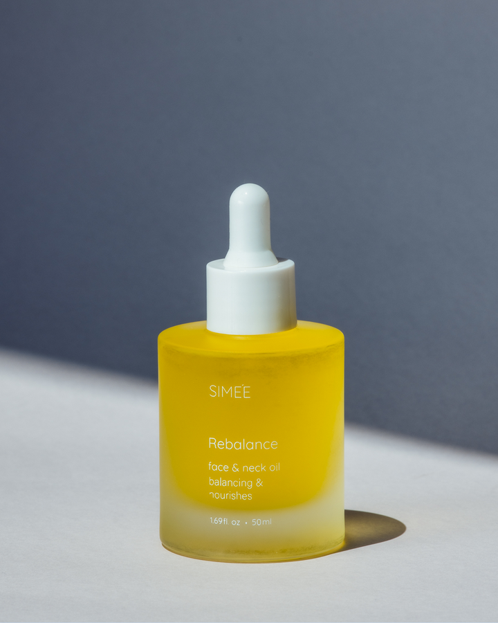 Dropper bottle of SIMÉE Rebalance face oil on a textured grey surface with a shadow cast to the side